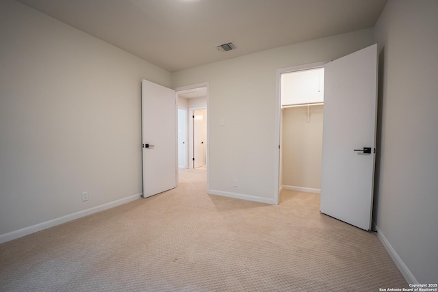 unfurnished bedroom featuring baseboards, a walk in closet, visible vents, and light colored carpet