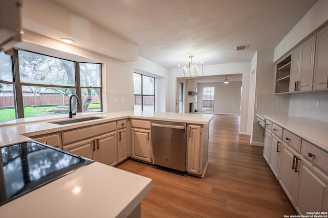 kitchen with a peninsula, stainless steel dishwasher, a sink, and light countertops