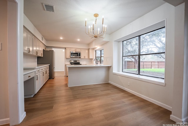 kitchen featuring stainless steel appliances, a peninsula, visible vents, light countertops, and decorative light fixtures