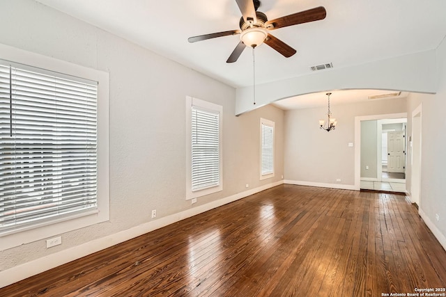 spare room featuring dark wood-style floors, arched walkways, visible vents, baseboards, and ceiling fan with notable chandelier