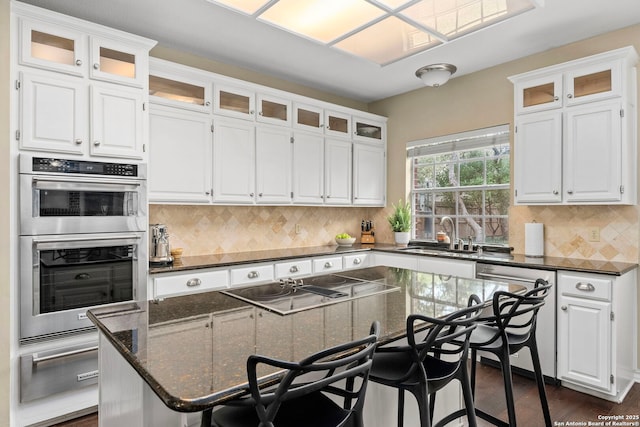 kitchen with dark stone counters, glass insert cabinets, a kitchen island, and white cabinetry