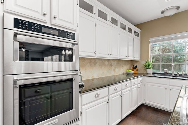 kitchen featuring stainless steel double oven, a sink, glass insert cabinets, and white cabinetry