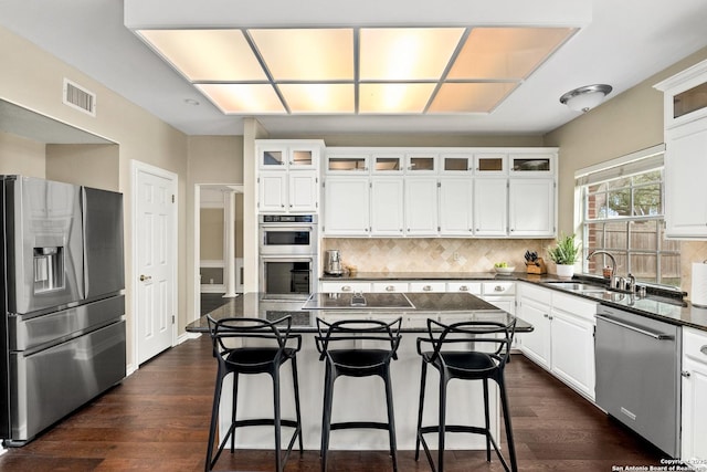 kitchen with a kitchen island, visible vents, white cabinets, appliances with stainless steel finishes, and glass insert cabinets