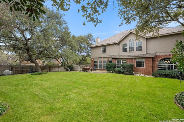 back of property with brick siding, a chimney, a fenced backyard, and a lawn