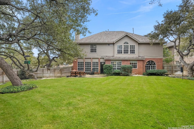 rear view of property with a chimney, brick siding, a lawn, and a fenced backyard