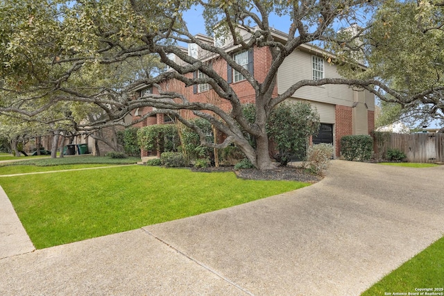 view of front of home featuring driveway, brick siding, fence, and a front yard