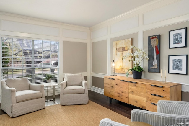 living area with ornamental molding, a decorative wall, and wood finished floors