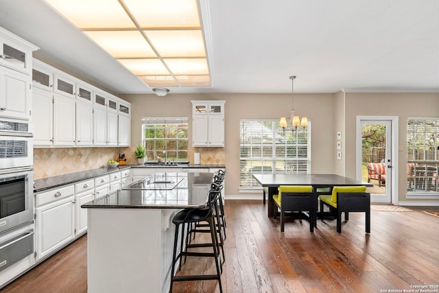 kitchen with a kitchen island, white cabinetry, a warming drawer, a kitchen bar, and glass insert cabinets