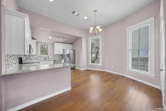 kitchen with light stone counters, visible vents, white cabinetry, hanging light fixtures, and appliances with stainless steel finishes