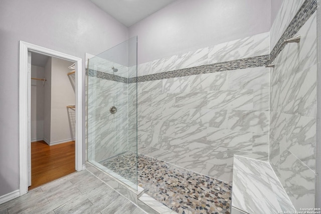 bathroom featuring a walk in shower, baseboards, a walk in closet, and wood tiled floor