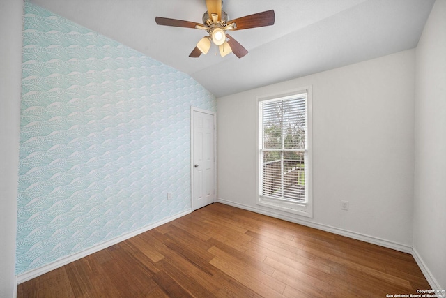 spare room with ceiling fan, wood finished floors, baseboards, vaulted ceiling, and wallpapered walls