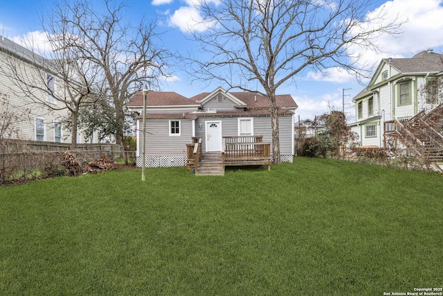 rear view of house with a yard, a wooden deck, and fence