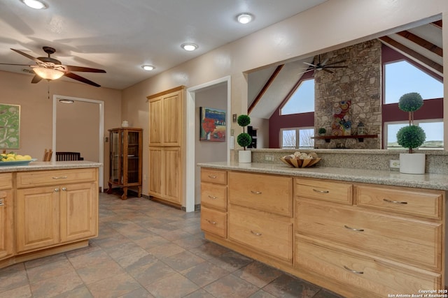 kitchen with vaulted ceiling, light stone counters, light brown cabinets, and a ceiling fan