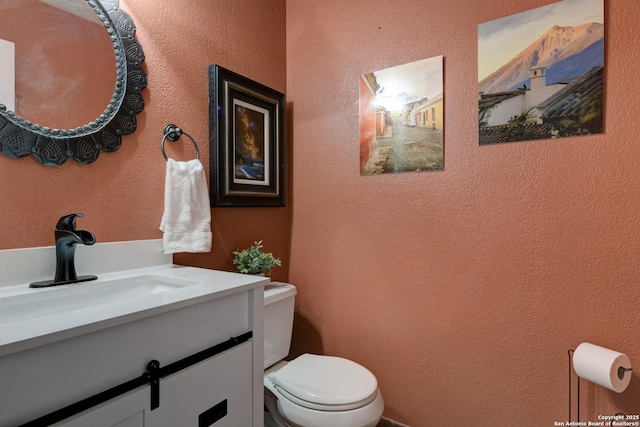 bathroom featuring toilet, a textured wall, and vanity