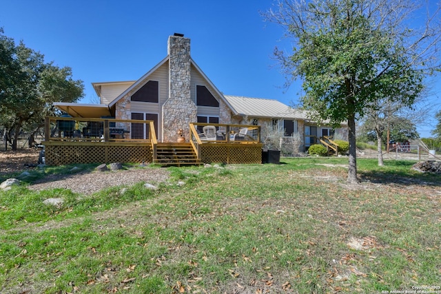 rear view of property featuring stone siding, a chimney, a wooden deck, and a lawn