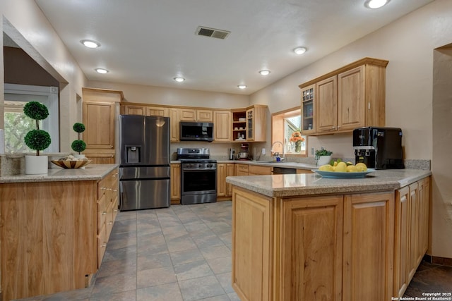 kitchen with light brown cabinets, a peninsula, visible vents, appliances with stainless steel finishes, and glass insert cabinets