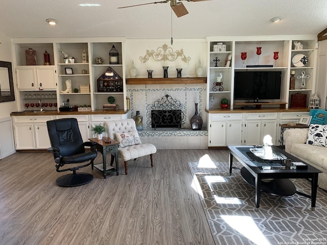 living area featuring a textured ceiling, a tile fireplace, a ceiling fan, and light wood-style floors