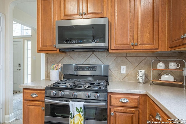 kitchen featuring brown cabinets, decorative backsplash, stainless steel appliances, and light countertops