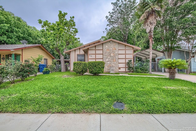 view of front of home with fence, stone siding, driveway, a detached carport, and a front yard