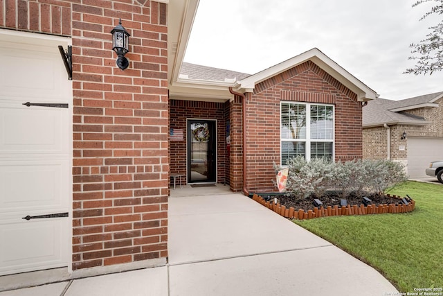 property entrance featuring a shingled roof, brick siding, a yard, and an attached garage