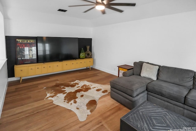 living room featuring ceiling fan, visible vents, baseboards, and wood finished floors