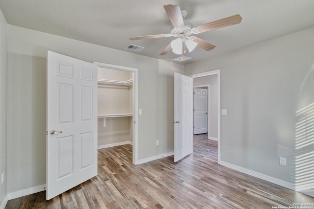 unfurnished bedroom with light wood finished floors, baseboards, visible vents, ceiling fan, and a walk in closet