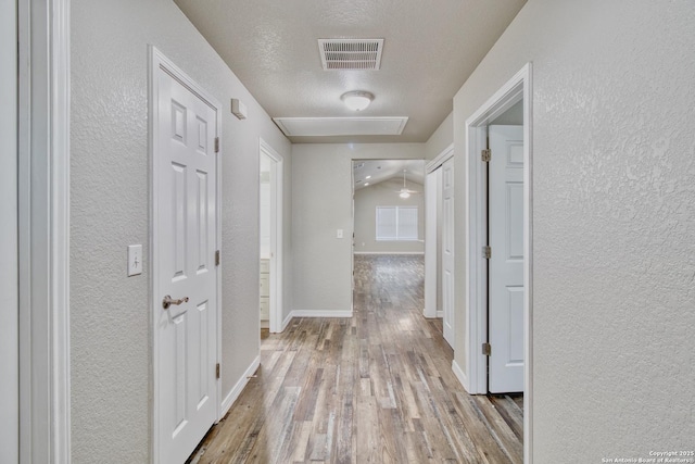 hall with a textured ceiling, a textured wall, light wood-type flooring, and visible vents