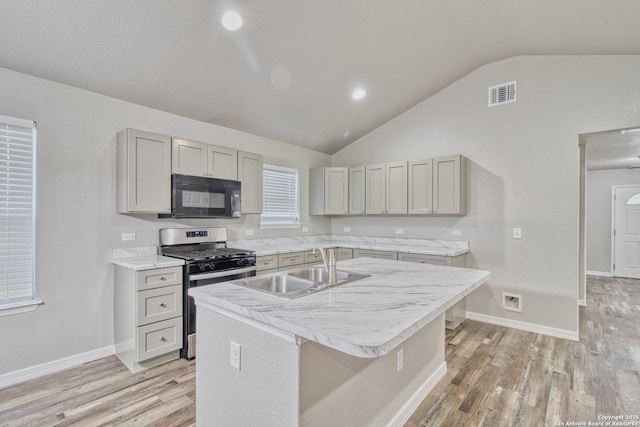 kitchen featuring black microwave, visible vents, light countertops, stainless steel range with gas cooktop, and a center island with sink