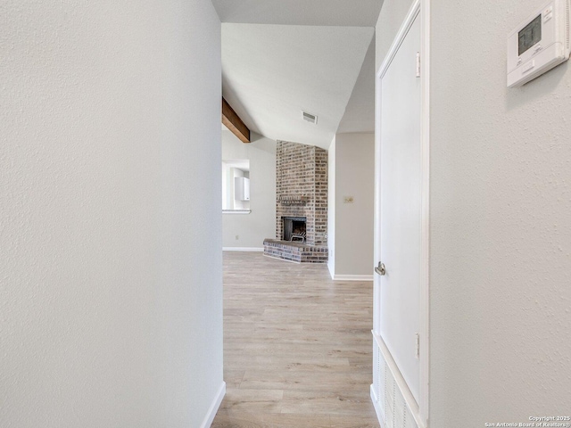 hallway featuring visible vents, vaulted ceiling with beams, light wood-style flooring, and baseboards