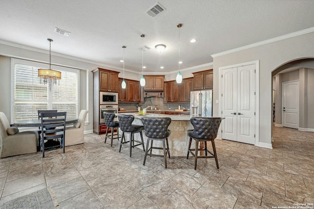 kitchen featuring arched walkways, an island with sink, a breakfast bar area, hanging light fixtures, and stainless steel appliances