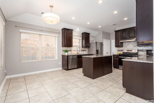 kitchen featuring light tile patterned floors, a sink, a kitchen island, appliances with stainless steel finishes, and light stone countertops