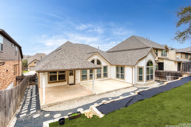 rear view of property featuring a shingled roof, a patio area, a lawn, and a fenced backyard