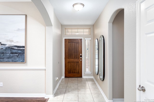 foyer with light tile patterned floors, baseboards, and arched walkways