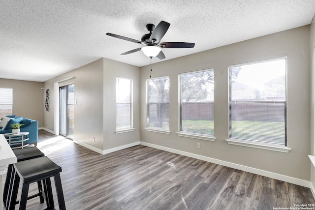 interior space with a ceiling fan, a textured ceiling, baseboards, and wood finished floors