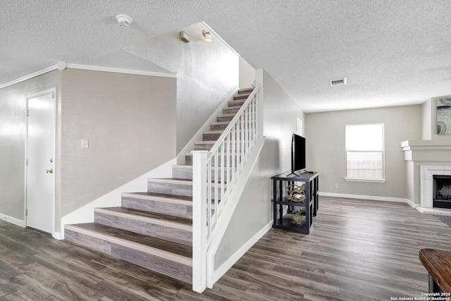 staircase with a fireplace with raised hearth, wood finished floors, visible vents, and baseboards