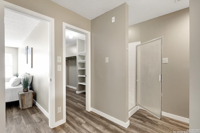 corridor featuring a textured ceiling, baseboards, and wood finished floors