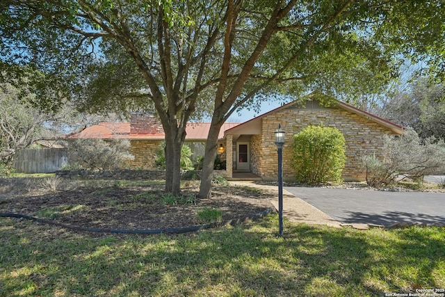 single story home featuring stone siding, fence, metal roof, and a front yard