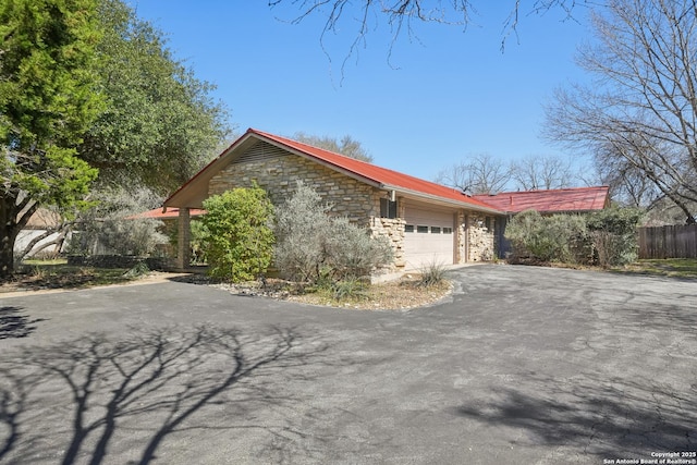 view of property exterior featuring metal roof, fence, a garage, stone siding, and driveway