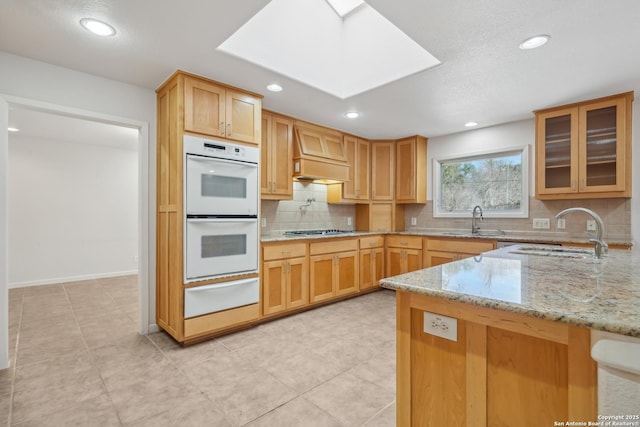 kitchen with light stone counters, a skylight, a warming drawer, double oven, and a sink