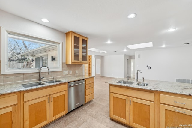 kitchen with stainless steel dishwasher, a sink, glass insert cabinets, and decorative backsplash