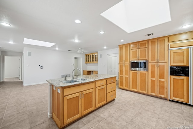 kitchen with a skylight, visible vents, a sink, an island with sink, and built in appliances