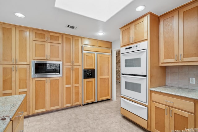 kitchen with light stone counters, a warming drawer, tasteful backsplash, visible vents, and built in appliances