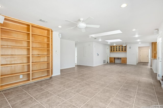 unfurnished living room featuring ceiling fan, built in shelves, a skylight, visible vents, and baseboards