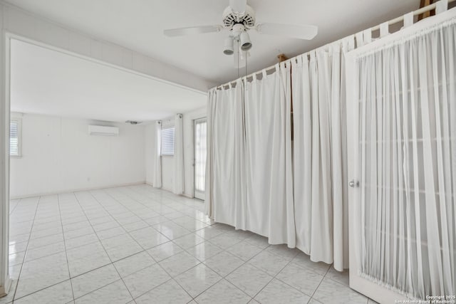 empty room featuring light tile patterned floors, a wall unit AC, and a ceiling fan