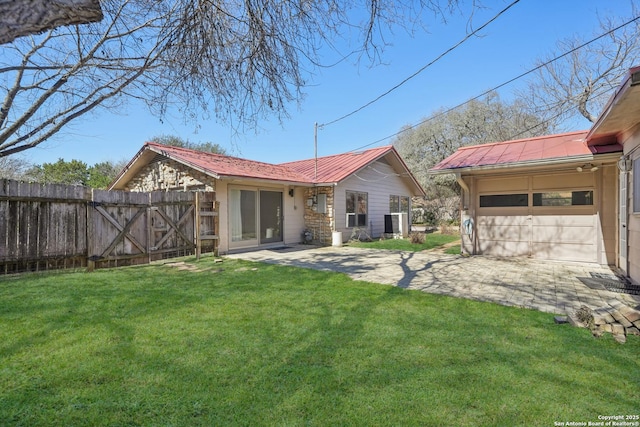 back of property featuring driveway, a garage, metal roof, fence, and a yard