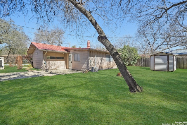 view of yard with driveway, an attached garage, fence, an outdoor structure, and a shed