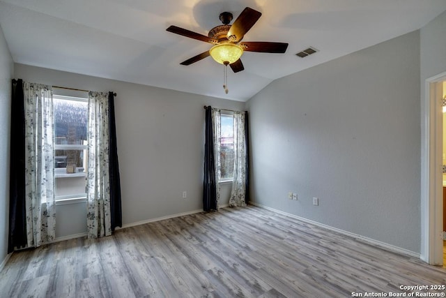 empty room featuring vaulted ceiling, visible vents, plenty of natural light, and light wood-style flooring