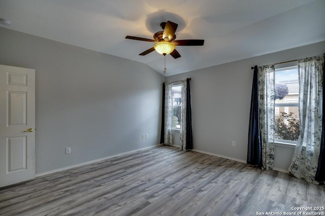 spare room with a healthy amount of sunlight, light wood-style flooring, baseboards, and vaulted ceiling