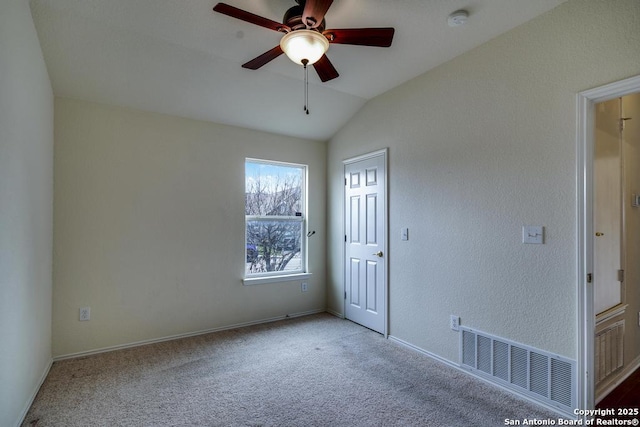 spare room featuring light colored carpet, visible vents, a ceiling fan, vaulted ceiling, and baseboards