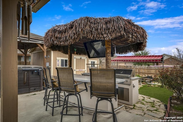 view of patio / terrace featuring exterior bar, area for grilling, fence, a grill, and a hot tub